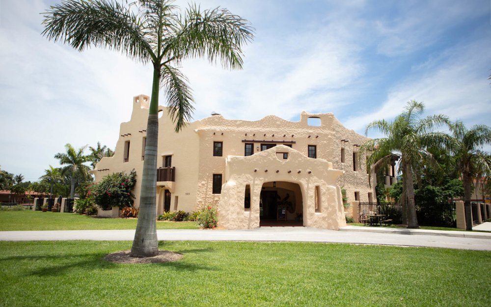 Vista exterior do Curtiss Mansion , exibindo sua arquitetura histórica com jardins exuberantes e palmeiras ao redor