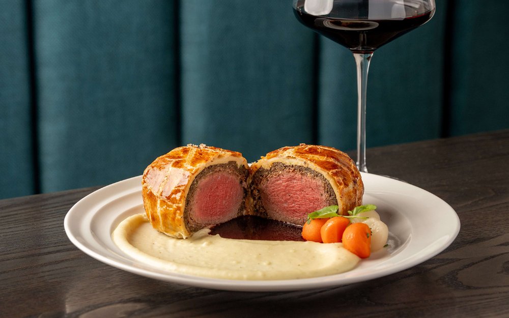 Beef Wellington, featuring a golden, flaky pastry crust, tender beef center, and a side of vibrant vegetables with mashed potatoes