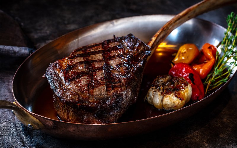 Bistecca cotta servita con aglio intero arrostito e peperoni, elegantemente impiattata