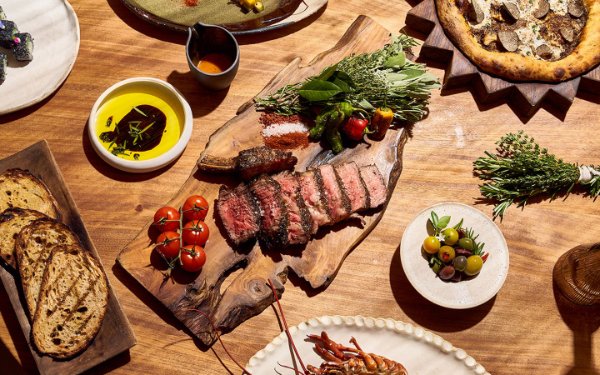 Uma deliciosa refeição em Casa Neos com bife, lagosta, acompanhamentos variados, Fresh tomates, azeitonas, pão fatiado e uma deliciosa pizza