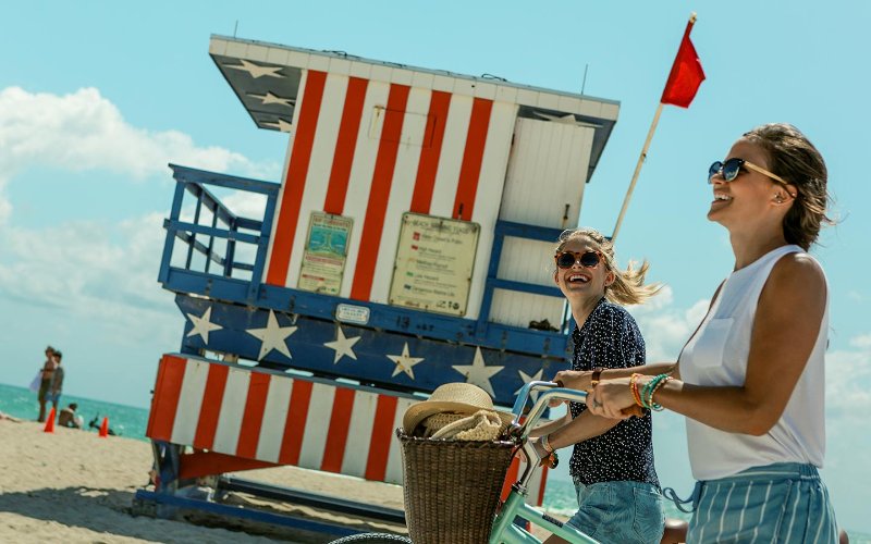Freunde schieben ihre Fahrräder an einem patriotischen Rettungsschwimmerstand vorbei Miami Beach
